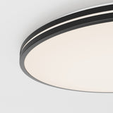 Close-up view of a modern, circular ceiling light fixture with a smooth, white illuminated surface and a thin, black trim against a white ceiling.