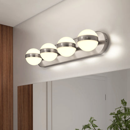 A modern wall-mounted bathroom light fixture with four round, frosted glass globes and metallic accents is installed above a large mirror. The reflection shows part of a green plant on the counter below.