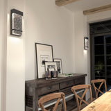 A rustic dining room with a wooden table and chairs, a console table against the wall with framed art and candles, and two modern wall sconces providing soft lighting. Natural light comes from a glass door.