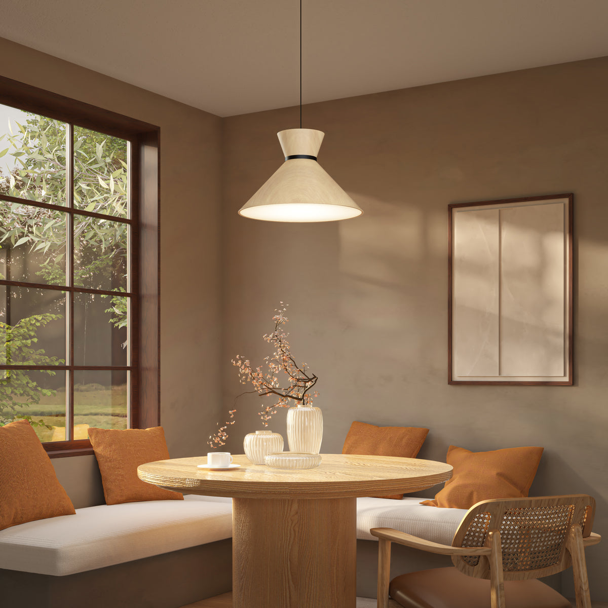 A cozy dining nook with a round wooden table, beige banquette seating with orange cushions, a rattan chair, ceramic vases with branches, a large window, and a pendant lamp hanging above.