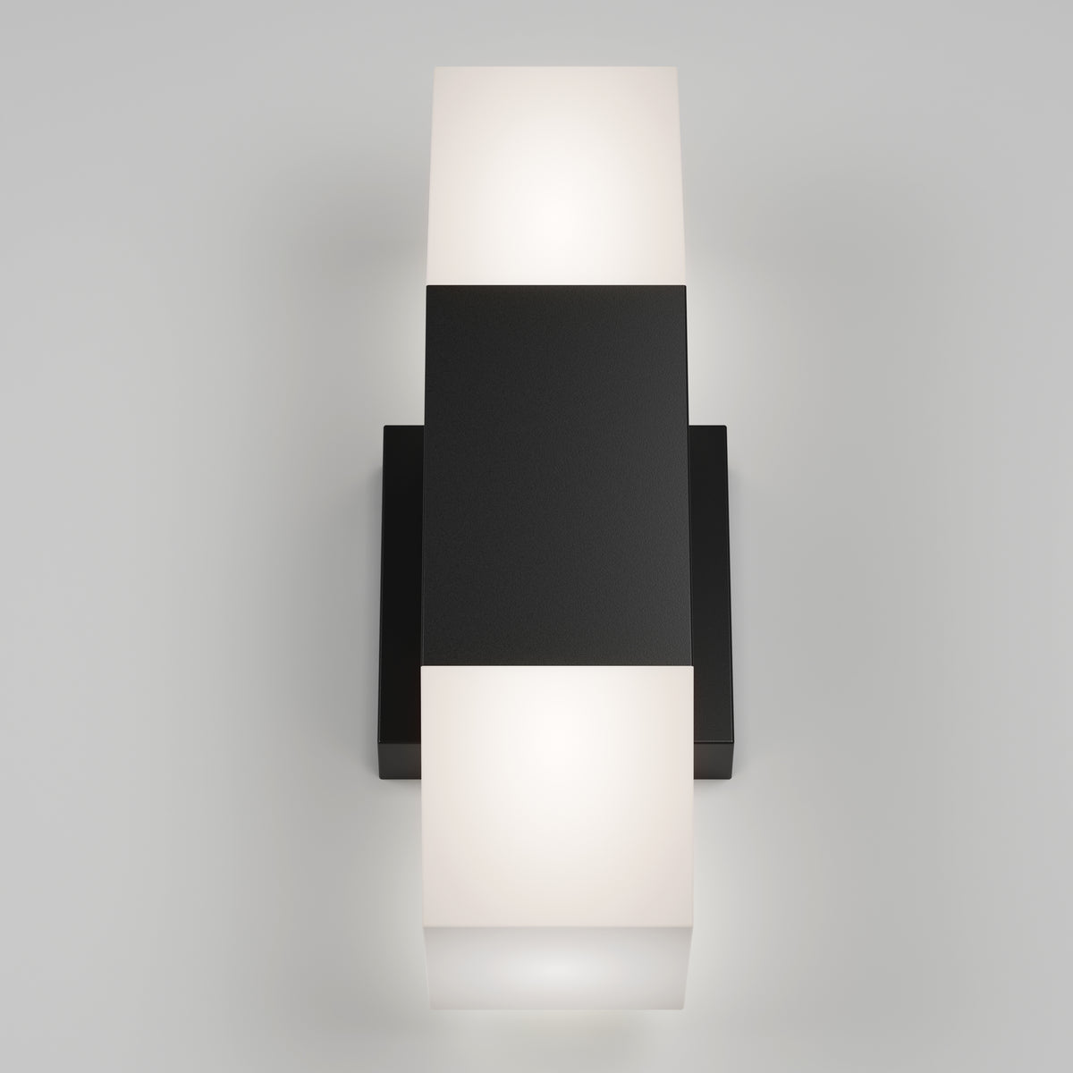 A modern wall light fixture with a central black rectangular base and two frosted white rectangular lamps, one above and one below, emitting soft light against a plain gray background.