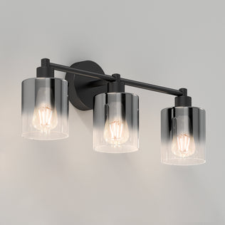 The Artika Haze modern 3-light bathroom vanity light features three exposed bulbs in cylindrical clear glass shades, set on a black metal bar with a round backplate for wall mounting.