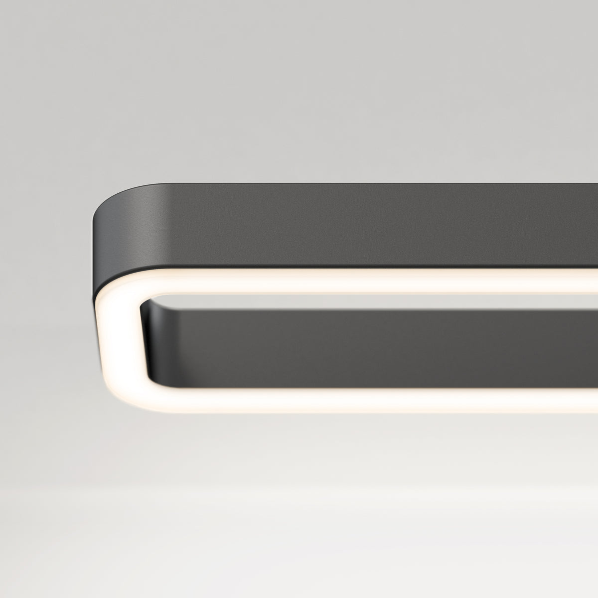 A close-up of a modern, rectangular ceiling light fixture with rounded edges and a glowing white border against a plain, light gray background.