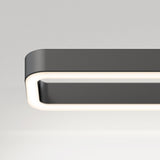 A close-up of a modern, rectangular ceiling light fixture with rounded edges and a glowing white border against a plain, light gray background.