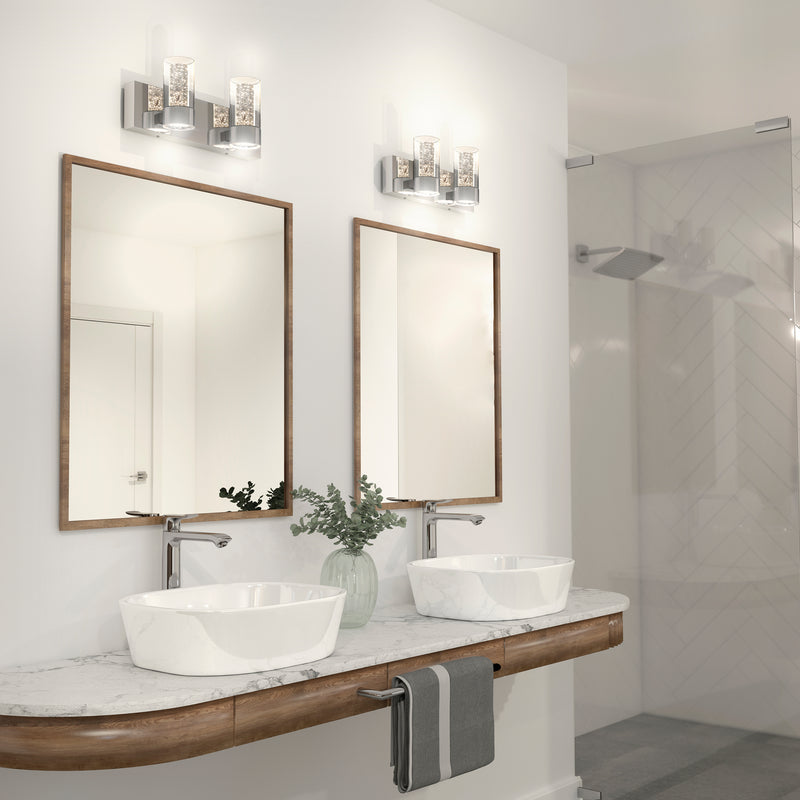 Modern bathroom with a double sink vanity, marble countertop, two framed mirrors, Artika Ratio 2-light LED vanity lights above each mirror, a white vase with greenery, and a glass-enclosed shower in the background.