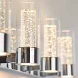 Close-up of modern cylindrical wall lights with chrome bases and clear glass shades containing bubbles, softly glowing against a neutral wall.