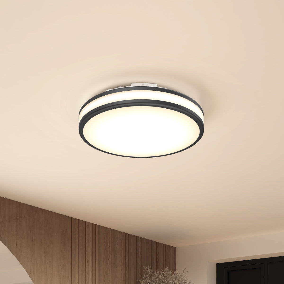 The Artika Hemisphere 15 in. LED flush mount light, featuring adjustable brightness and a black and white trim, is mounted on a beige ceiling in a minimalist room with wood paneling and an arched doorway.
