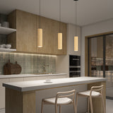 Modern kitchen with wooden cabinets, green tile backsplash, pendant lights above a white island with two stools, built-in ovens, open shelving with dishes, and a large window showing a snowy outdoor scene.