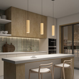 Modern kitchen with textured wood cabinets, green tile backsplash, and a white island with two light stools. Three Artika Groove LED modern pendant lights (3 CCT) illuminate the island while a large window reveals a snowy view.