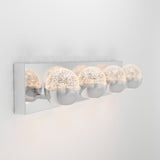 A modern wall-mounted light fixture with four round, half-chrome, half-textured glass bulbs attached to a shiny rectangular metal base, glowing softly against a white wall.
