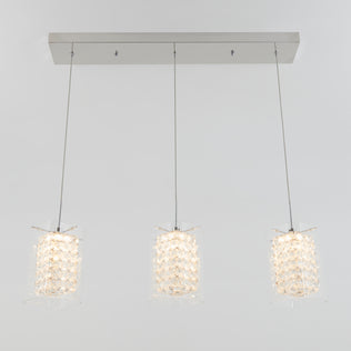The Artika Crystal Cube 3-light LED pendant light features three crystal cube shades hanging in a row from a rectangular metallic mount, suspended by thin cables against a plain light gray background.