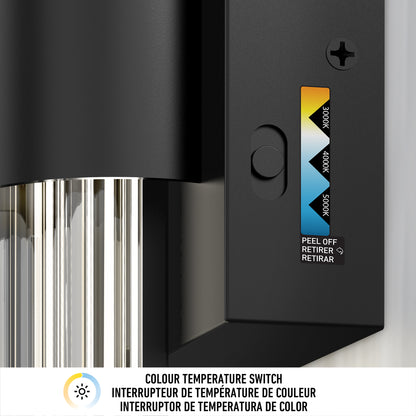 Close-up of Artikas Dorado LED contemporary wall sconce 3 CCT in black, featuring a color temperature switch for 3000K, 4000K, and 5000K. A peel-off sticker is beside the switch. Multilingual text appears below in English, French, and Spanish.