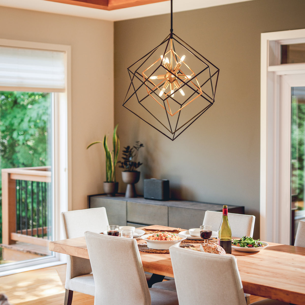 Modern dining room with wood table, white chairs, Artika Imperium 9-light LED chandelier, food served, big windows, and plants.