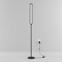 The Artika Leni dimmable LED modern floor lamp features an oval light and flat base, standing plugged into a wall outlet against a plain light gray background.