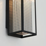 A modern wall sconce with a black metal frame and perforated metal panels, allowing light to shine through the small circular holes, mounted on a white wall.