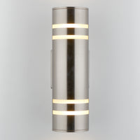 The Artika Voltz indoor-outdoor wall light is a modern cylindrical sconce in brushed metal, featuring horizontal frosted light strips glowing at the top and bottom, mounted vertically against a light gray background.