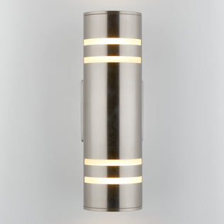 The Artika Voltz indoor-outdoor wall light is a modern cylindrical sconce in brushed metal, featuring horizontal frosted light strips glowing at the top and bottom, mounted vertically against a light gray background.