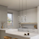 Modern kitchen with white cabinets and countertops, three spiral pendant lights, a window with blinds, minimalist decor, and a coffee press on the counter. Natural light brightens the clean, neutral space.