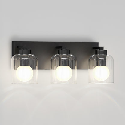 Artika Aryna 20 in. 3-Light LED Vanity, black base with clear glass shades, glows warmly on a white wall.