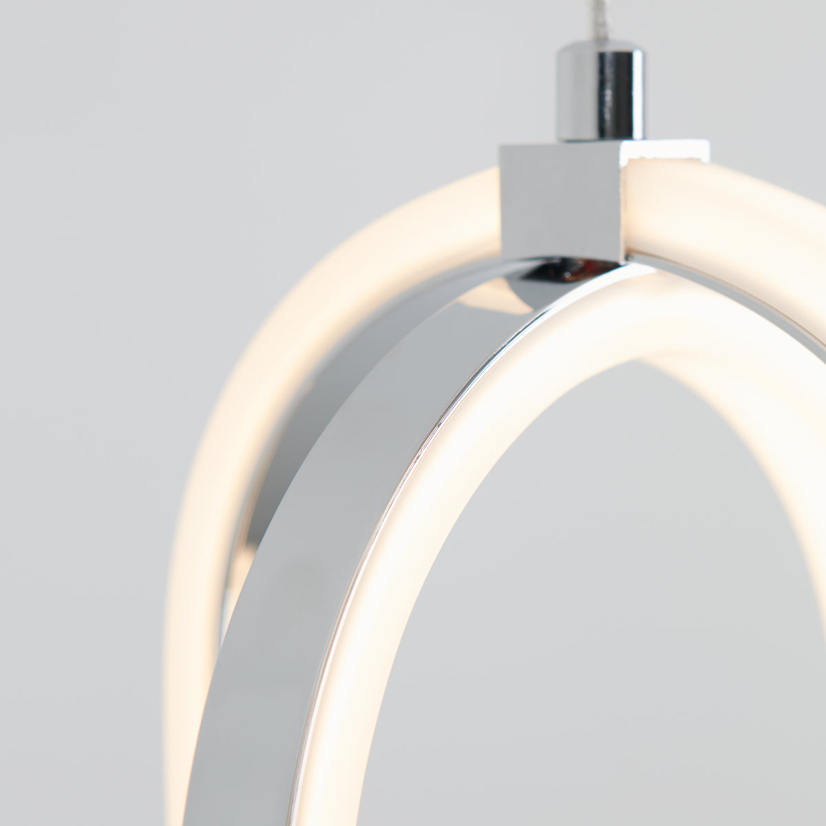 Close-up of a modern, minimalist pendant light with curved, chrome metal and glowing LED strips, set against a plain light gray background.