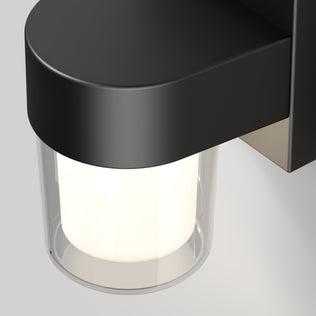 A close-up of the Halden indoor-outdoor LED wall light by Artika, featuring a matte black finish and cylindrical frosted glass shade, gently illuminates the area with adjustable 5 CCT lighting.