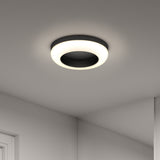 Modern circular ceiling light fixture with a glowing white ring and a dark central area, mounted on a smooth, light-colored ceiling with part of a wall and doorframe visible.