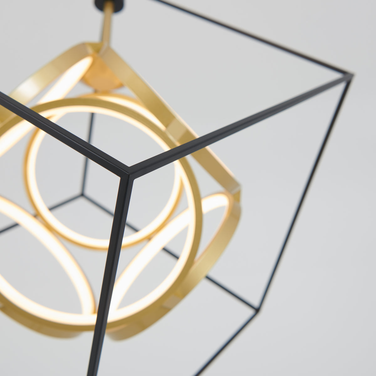 A modern pendant light featuring a black geometric cube frame with glowing circular LED elements and gold accents, suspended against a plain, light background.