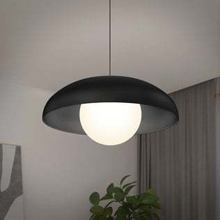 The Artika Boden LED modern mid-century pendant light 3 CCT, featuring a black dome-shaped shade and glowing white globe, hangs from the ceiling with a green plant and curtain in the background.