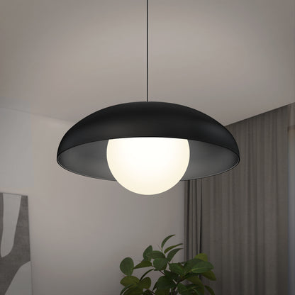 The Artika Boden LED modern mid-century pendant light 3 CCT, featuring a black dome-shaped shade and glowing white globe, hangs from the ceiling with a green plant and curtain in the background.