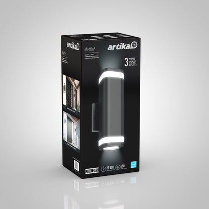 A black retail box for the Artika Mettle LED indoor-outdoor wall light features images of its cylindrical design with lit ends, showcases it installed outside a home, and highlights a 25,000-hour lifespan and 680 lumens.