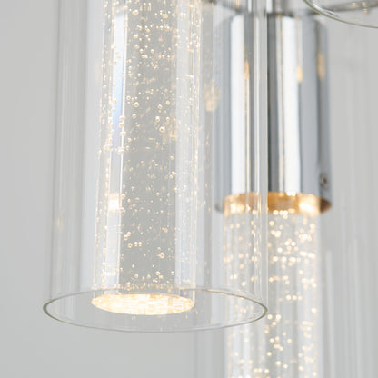 Close-up of Artika’s Bubble Swirl 5-light pendant, featuring modern cylindrical glass shades with bubbles and a sleek chrome finish, emitting a warm glow against a soft, neutral background.