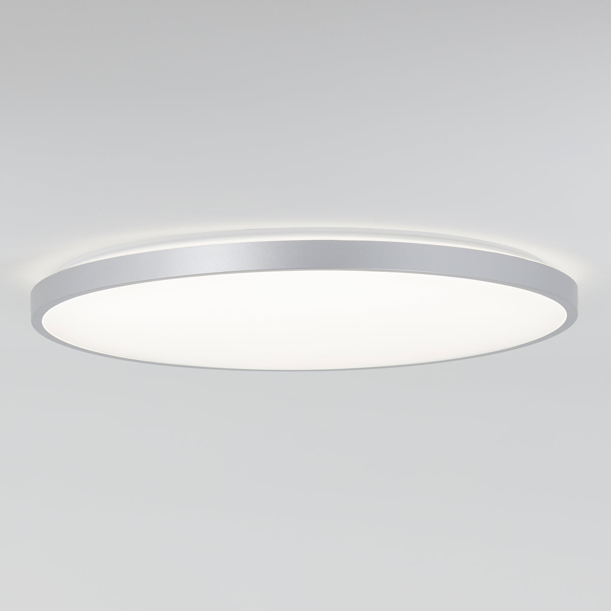 A modern, round, flush-mounted ceiling light with a white diffuser and a slim metallic frame, glowing softly against a plain white ceiling.
