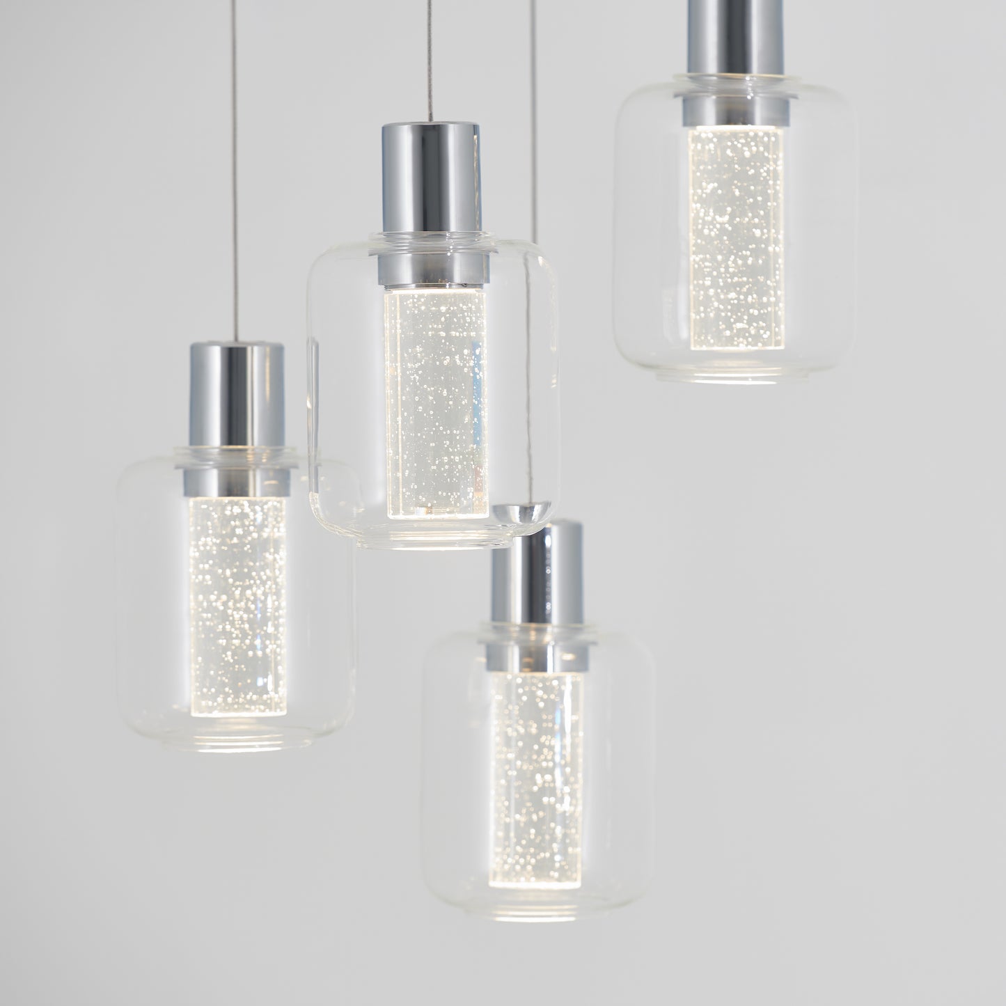 The Artika Champagne Globe 4-light LED pendant features four modern lights with cylindrical, bubble-dotted glass shades and metallic tops, elegantly suspended on thin wires against a plain light gray background.