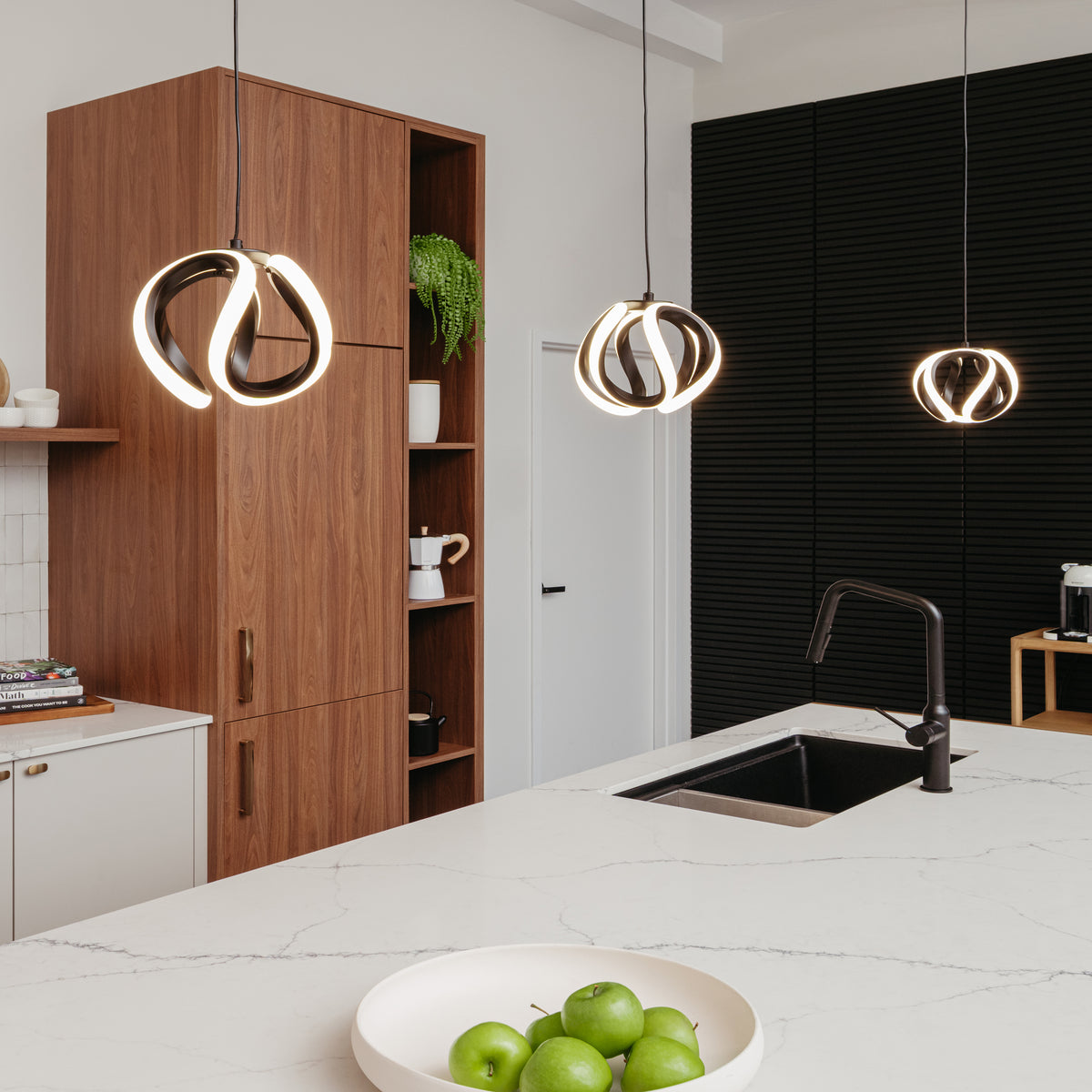 Modern kitchen with a white island, black sink, green apples in a bowl, wooden cabinets, potted plant, and three Artika Vivaldi LED pendant lights (3 CCT) hanging from the ceiling.