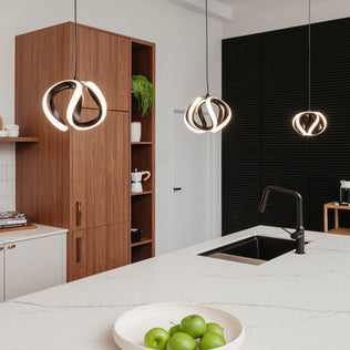 Modern kitchen with a white island, black sink, green apples in a bowl, wooden cabinets, potted plant, and three Artika Vivaldi LED pendant lights (3 CCT) hanging from the ceiling.