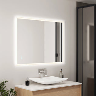 A modern bathroom features the Artika Mavis 48" x 36" rectangular LED mirror with defogger, a square white vessel sink on a wooden vanity, a chrome faucet, minimal accessories, and a plant in the corner.