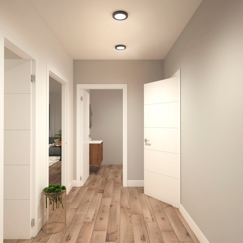 A bright hallway with light walls and wooden floors features three doorways and a small green plant. Illuminated by the Artika Europa Disk 7 in. LED modern flush mount light with 3 CCT for customizable lighting.