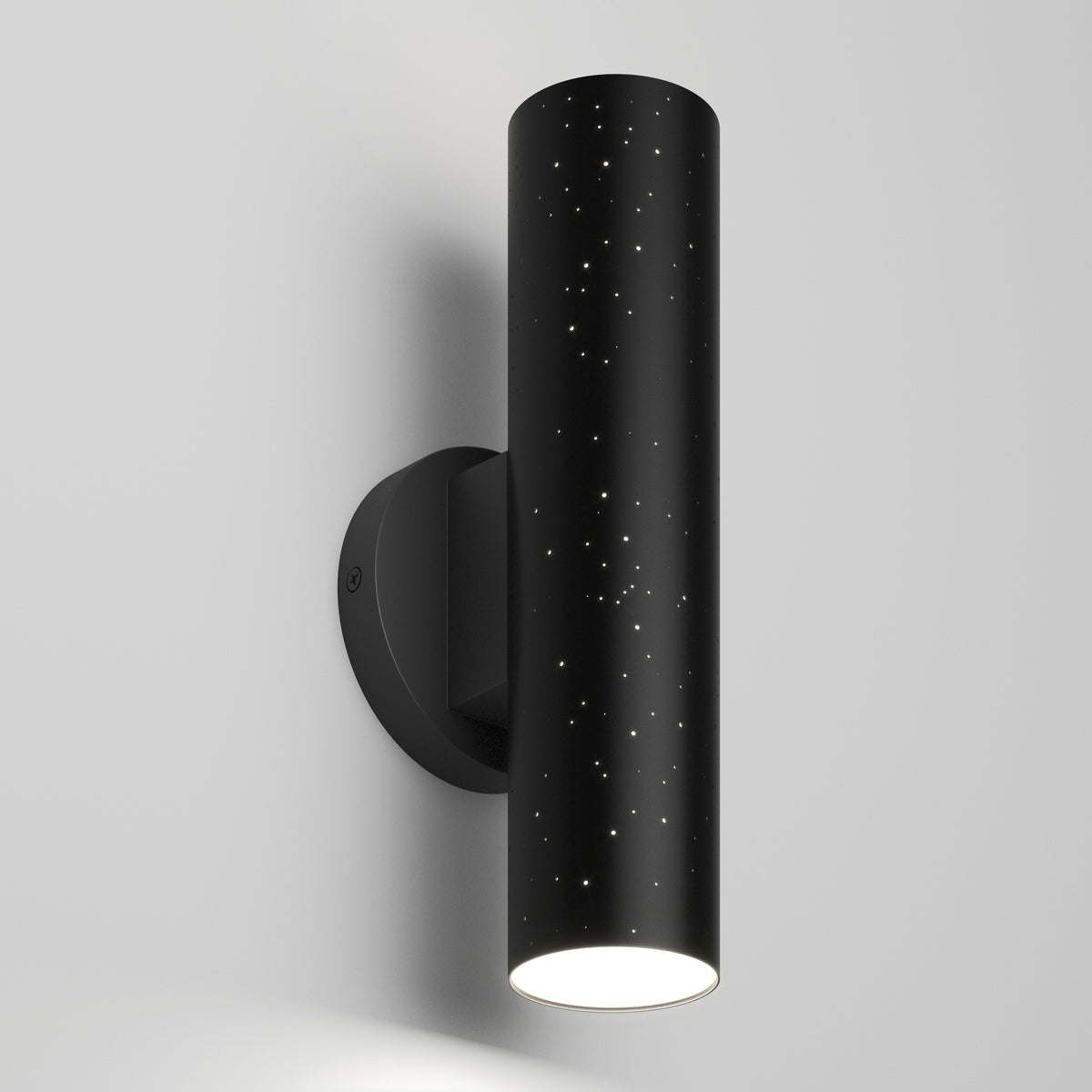 A modern black cylindrical wall sconce with tiny star-like perforations, mounted on a white wall, emits light from the bottom, creating a sleek and minimalist design.