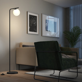 A modern living room with a beige sofa, dark green armchair, Artikas Clayton dimmable LED modern mid-century floor lamp, framed wall art, large window with sheer curtains, rug, and potted plant.