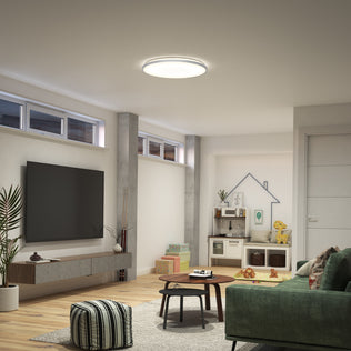 Modern living room with green sofa, TV, toy kitchen set, round table, and Artika Jupiter 23" LED flush mount light with remote.