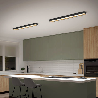 Modern kitchen with green cabinets, wood accents, a white island with two gray bar stools, built-in oven, sink, and two Artika Alton 48 in. LED flush mount lights on the ceiling. A window with a white blind is on the left wall.