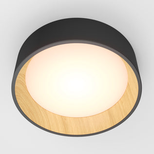 The Artika Alton LED flush mount features a round black outer frame, wooden inner rim, and glowing white center—modern lighting for any room. Seen here from below against a plain white ceiling.
