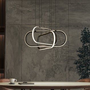 A modern dining area with a round table holding a cup, saucer, and book sits beneath the Artika Lewis modern LED pendant light 3 CCT. Textured gray walls and a leafy plant provide a stylish backdrop.