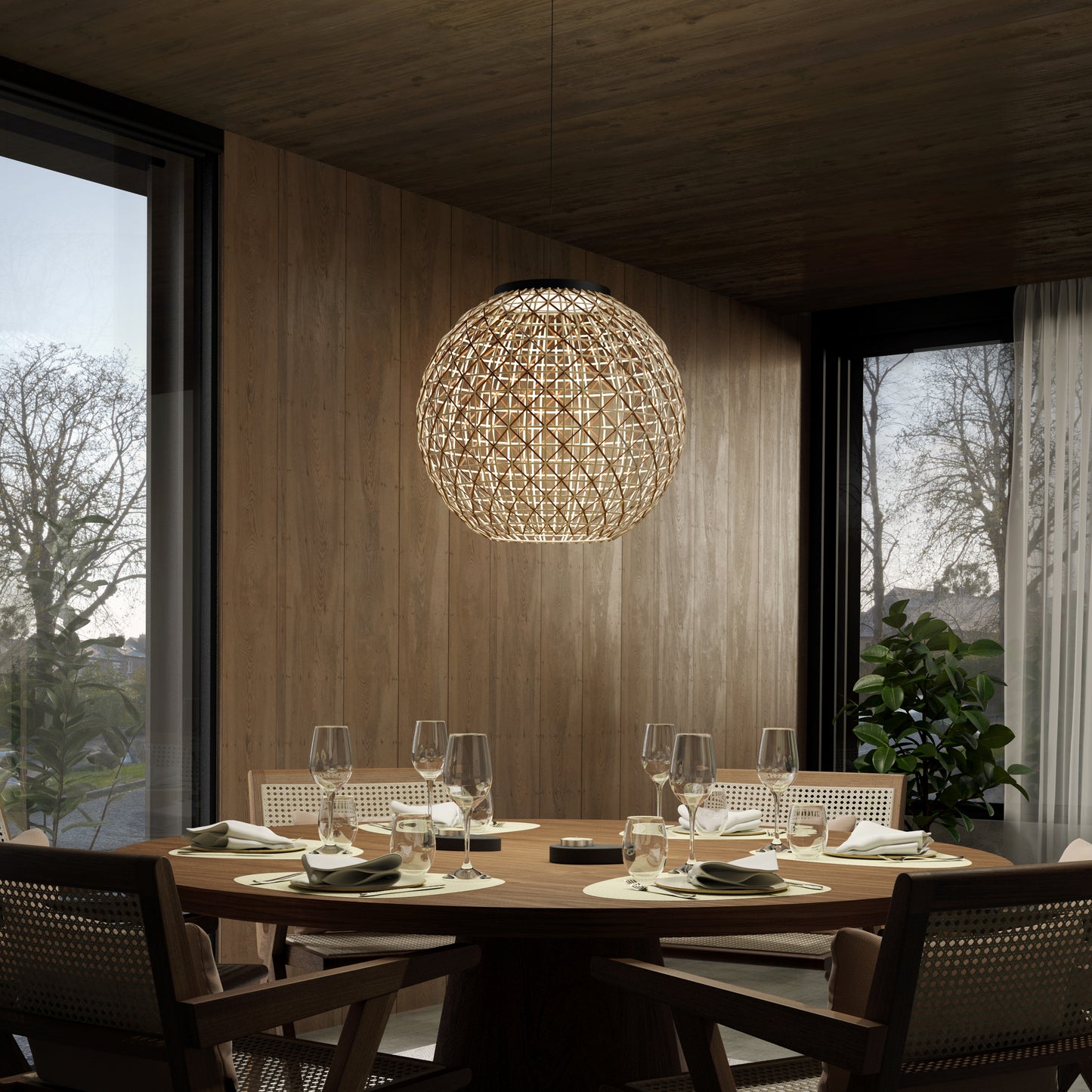 A modern dining room with a round wooden table set for six, featuring glassware and plates. Above hangs the Artika Benson LED pendant light 5 CCT, with large windows and a potted plant in the background.