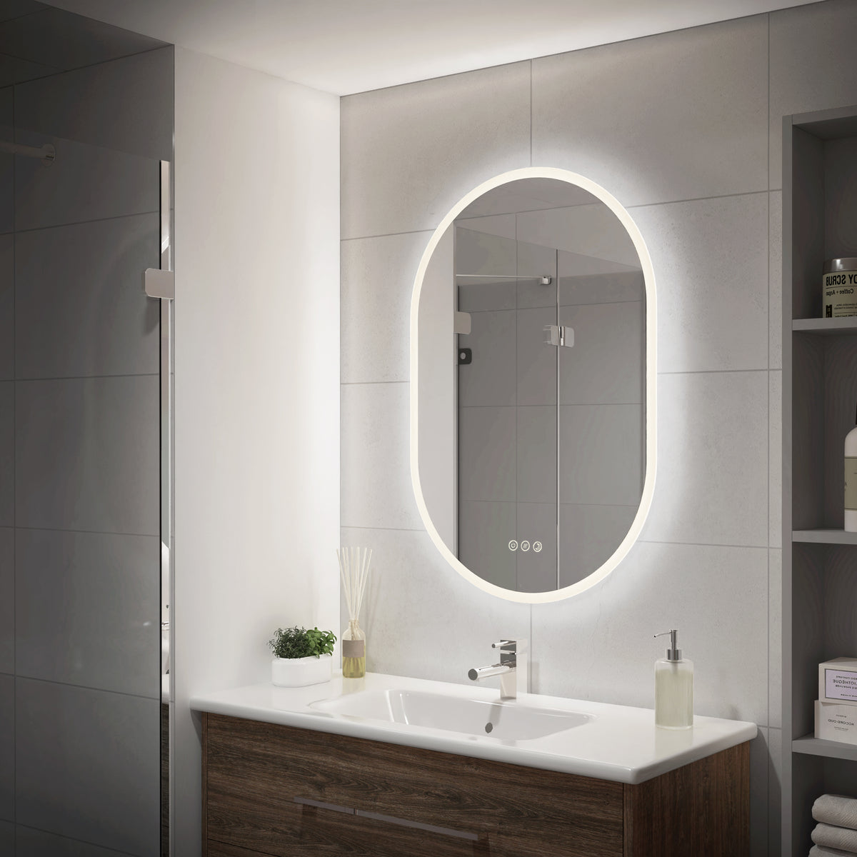 Modern bathroom with Artika Clara 30″x20″ oval LED mirror, white sink, wood cabinet, plant, soap dispenser, and toiletry shelves.