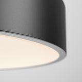 A close-up of a modern, round, black ceiling light fixture with a smooth surface, emitting a soft, warm glow against a plain, light gray background.
