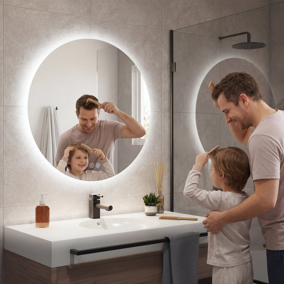 A man and a young boy smile while brushing their hair in front of the Artika Raya 24 in. LED mirror 3 CCT with defogger, featuring touch controls. The modern bathroom has a sink, soap dispenser, plant, and a glass shower in the background.