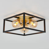 Modern ceiling light fixture with exposed bulbs, featuring a square black metal frame and a central brass base, mounted on a white ceiling. The bulbs emit a warm, ambient glow.