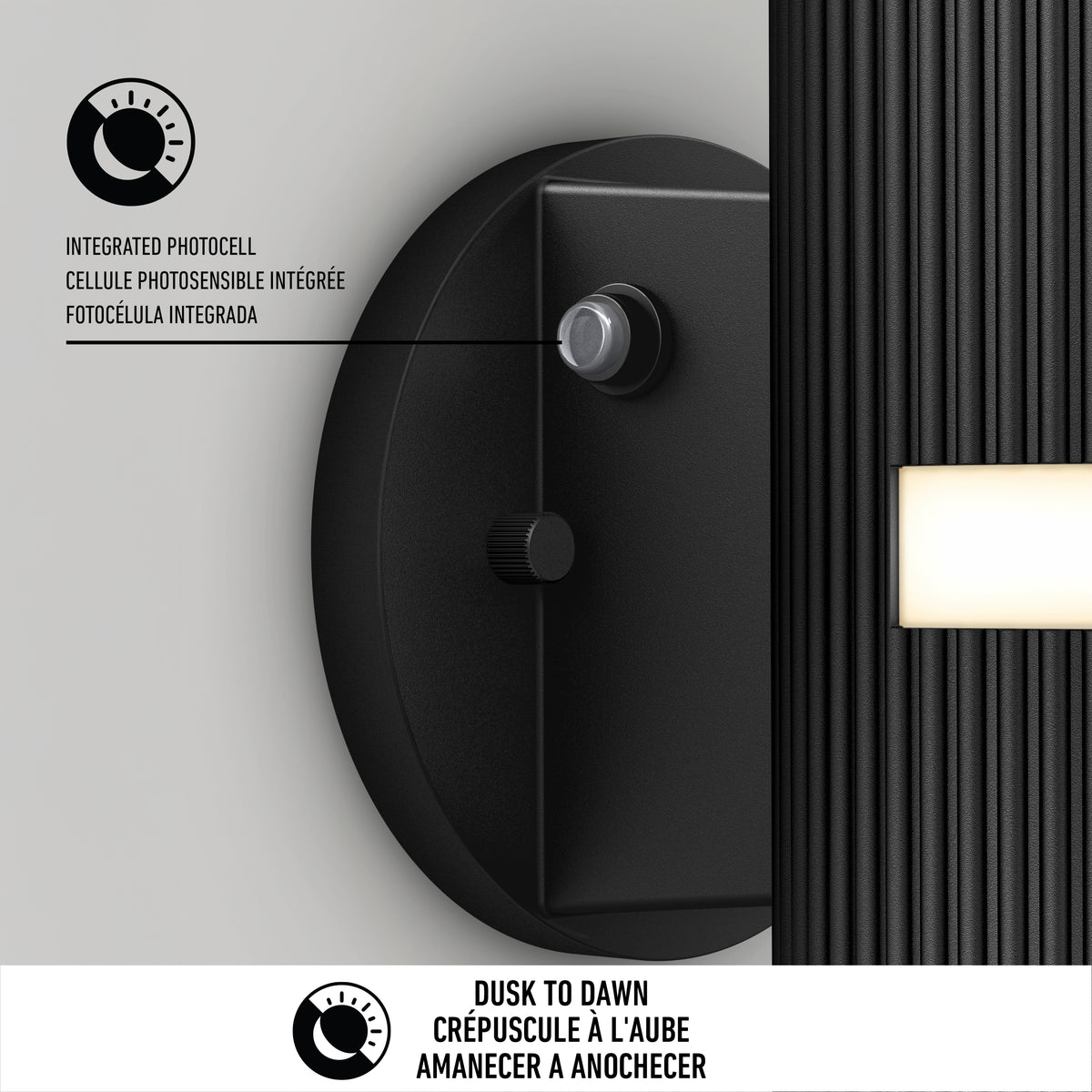 Close-up of a black outdoor light fixture showing its integrated photocell sensor. Text highlights Dusk to Dawn functionality in English, French, and Spanish, with icons and descriptions of the photocell feature.