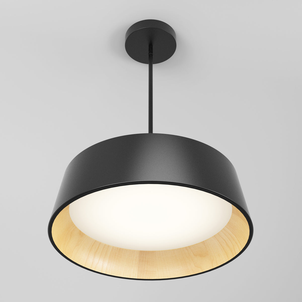 A modern ceiling pendant light with a black outer shade and a light wood-finished inner lining, suspended from a black rod against a plain white ceiling. The light is turned on, softly illuminating the interior.